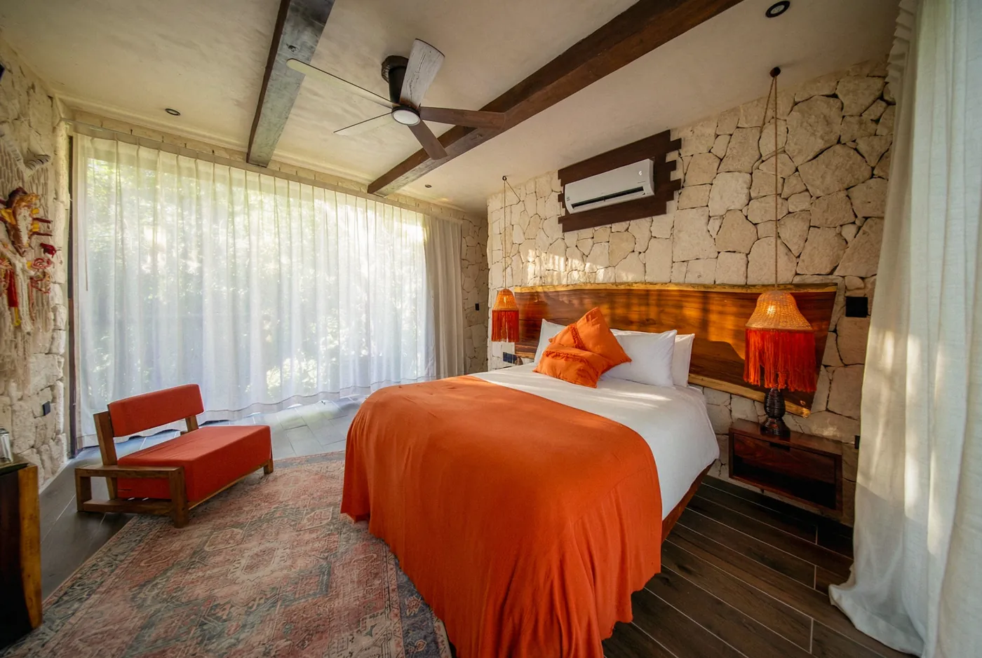 Queen room at Kaaba Luum with an orange throw, red armchair, and floor-to-ceiling windows